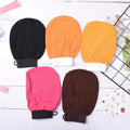 Five bath scrub gloves in black, orange, yellow, pink and dark brown arranged on a light surface.