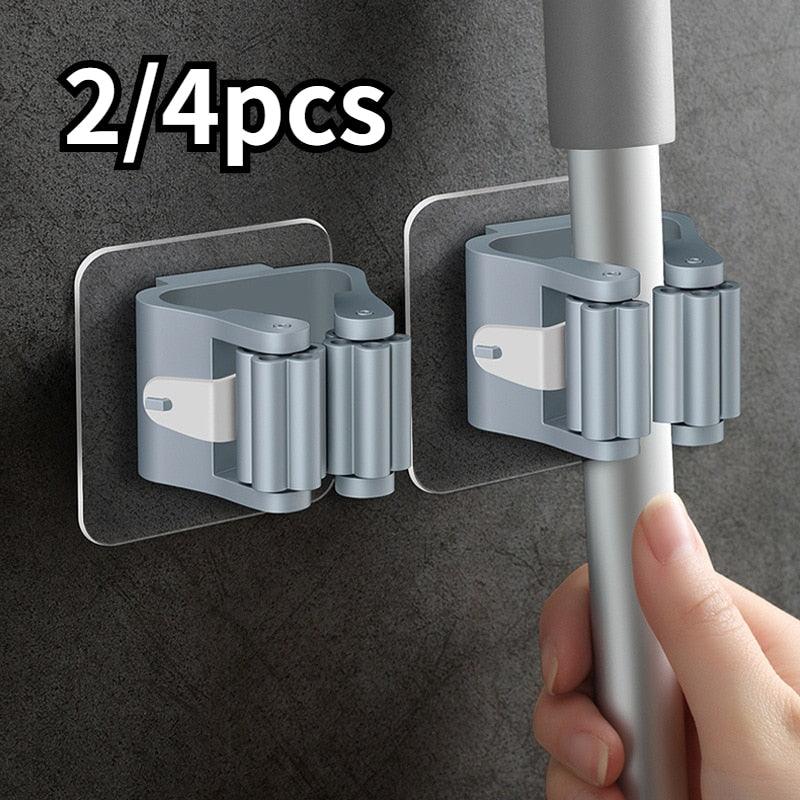 Two gray adhesive broom and mop holders gripping a pole against a dark textured wall.