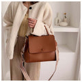 Person in a light jacket wearing a brown flap-style crossbody shoulder bag with a long patterned strap.