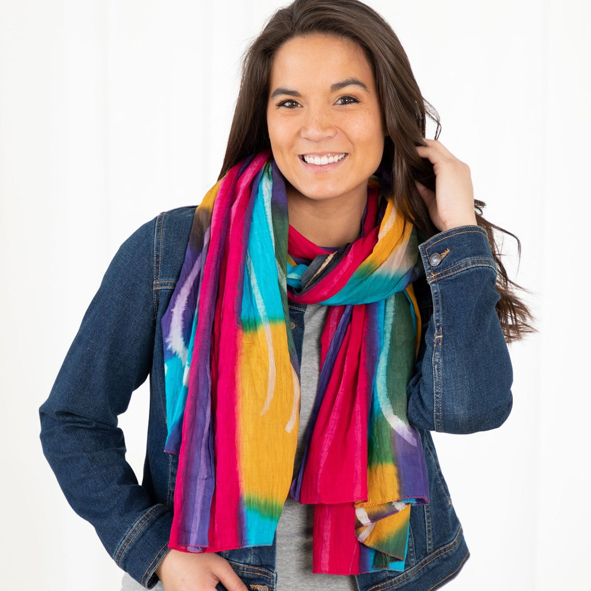 Smiling woman wearing a bright multicolored scarf over a denim jacket.
