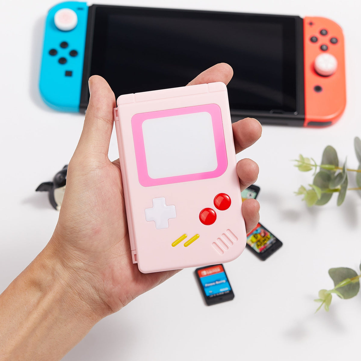Hand holding a pink retro game-console-shaped case in front of a Nintendo Switch and game cards.
