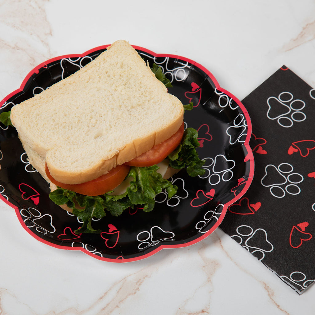 Black paw-print paper party plate holding a sandwich, with a matching napkin beside it.