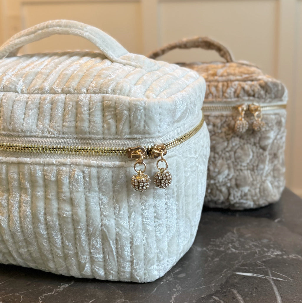 Quilted ivory vanity case with a top handle, zipper and gold-tone hanging charms, with another case behind.
