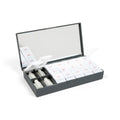 Open charcoal-gray pill organizer with white daily compartments, a mirror and small tablets.