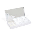 Open white weekly pill organizer with labeled daily sections, mirror and small tablets.