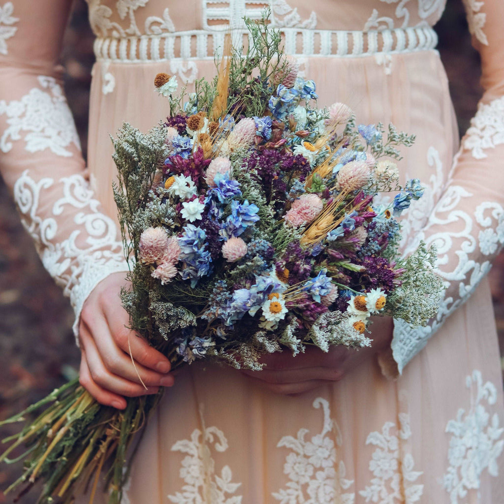 Person holding a mixed dried wildflower bouquet with blue, purple, pink and cream blossoms.