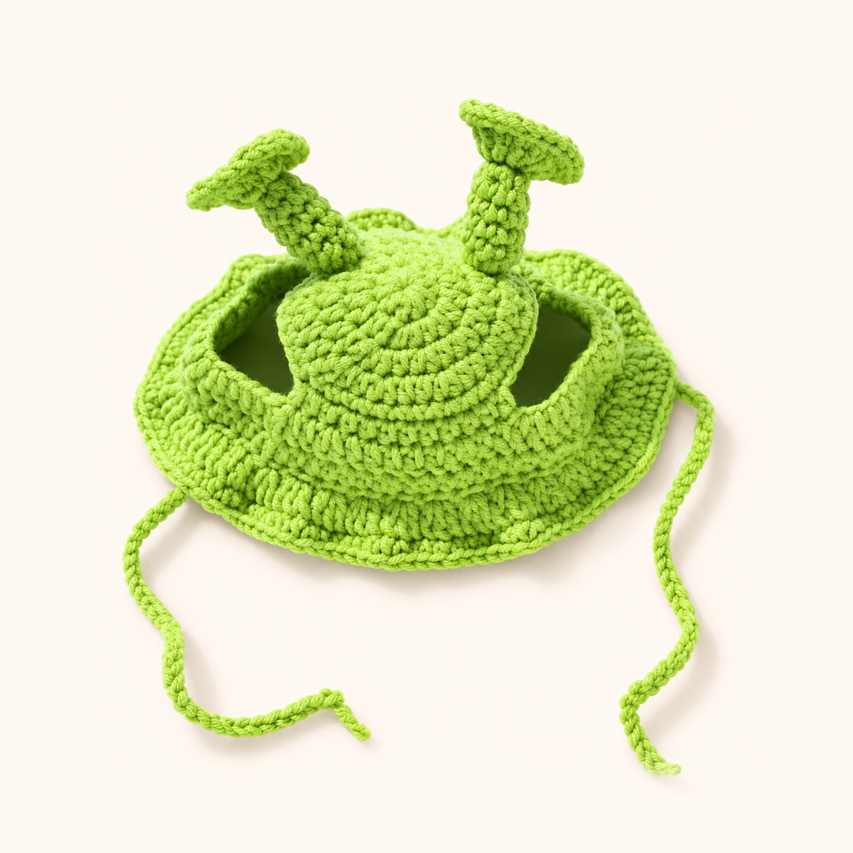 Lime green knitted cat and dog hat with two antennae and chin ties on a warm cream background.