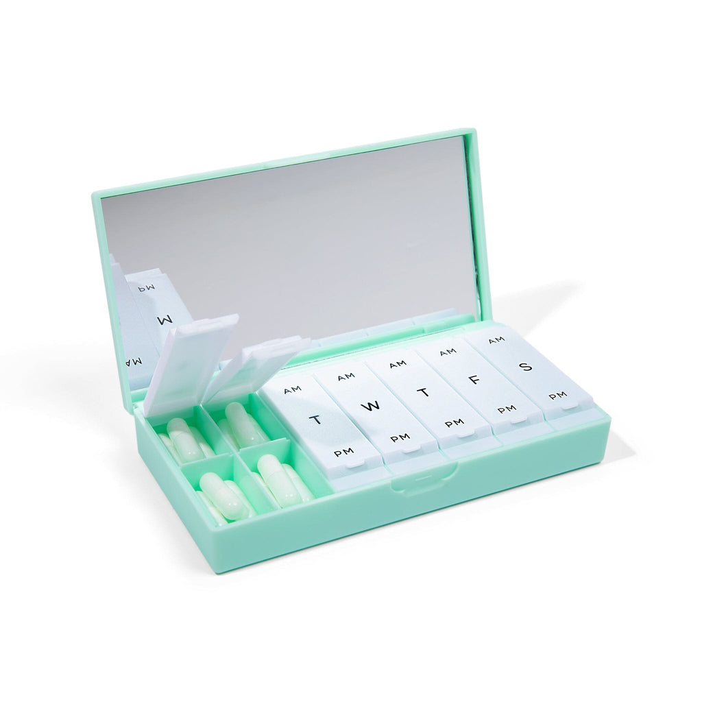Open mint-green weekly pill organizer showing labeled compartments, a lid mirror and tablets.